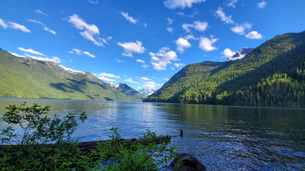 A calm mountain lake near Chilliwack, BC, ringed by forested slopes under a blue summer sky